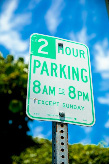 A circular no parking traffic sign with a red border and blue center featuring a red slash, mounted on a metallic pole casting a shadow on a textured brick wall made of light-colored and darker stones, with a horizontal band of red bricks near the bottom. The sign is positioned outdoors, indicating parking restrictions in the area, which is relevant to moving and home relocation services. The scene is well-lit, highlighting the details of the sign and the wall. In the context of Lewisham parking rules for SE3 removals explained by Man with Van Blackheath, this image illustrates parking limitations that must be considered during furniture transport and packing and moving activities in the area.